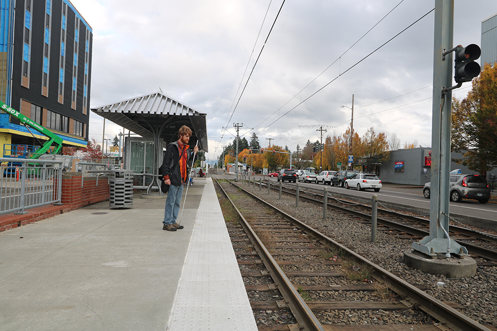 David stands still with his cane recording sounds while waiting for the Max train