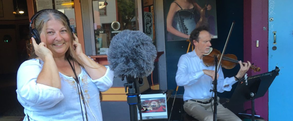 In this photo, multimedia storyteller, Mary Anne Funk, is listening to and recording spatial audio of a violin player in front of a movie theater in Portland, Oregon.