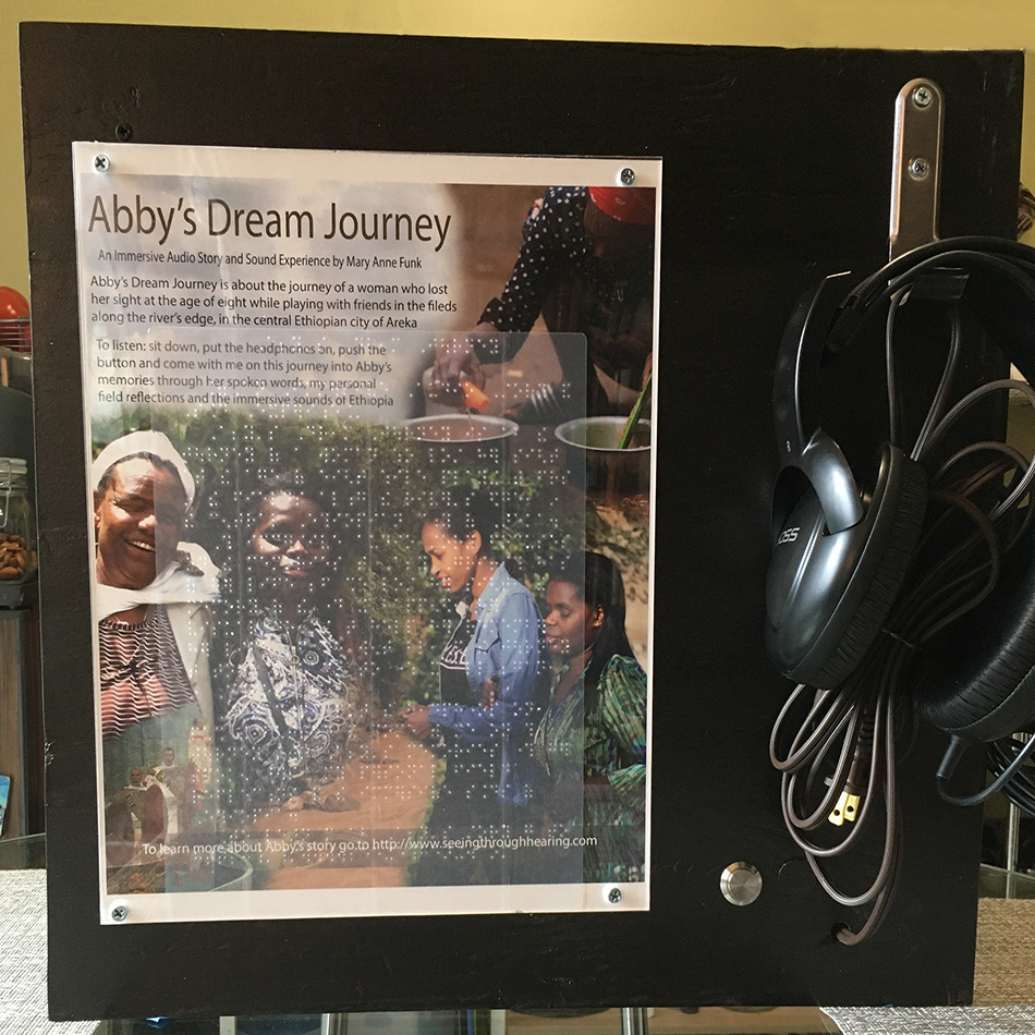 The interactive story box that Mary Anne's husband Mark created for the in-person story exhibit has headphones attached, a push button to listen to the story and a poster with braille overlay for people who are blind to read what the audio story is about.